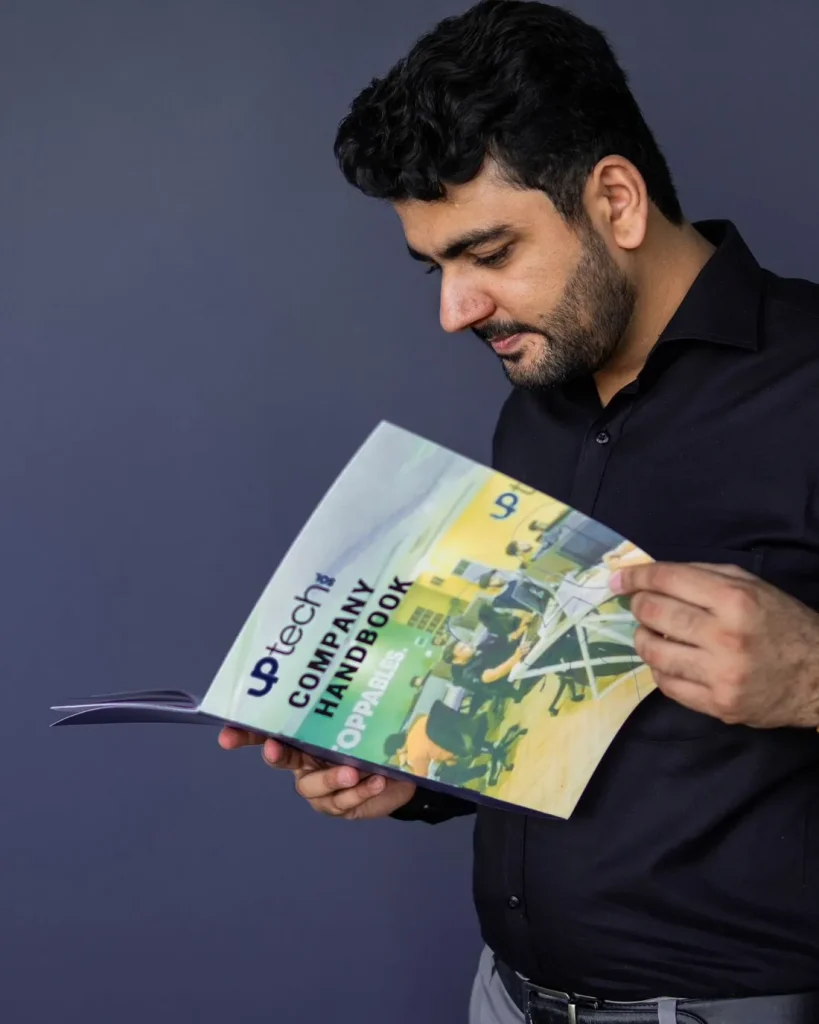 Umar Hameed in a black shirt reading a company handbook against a dark navy backdrop