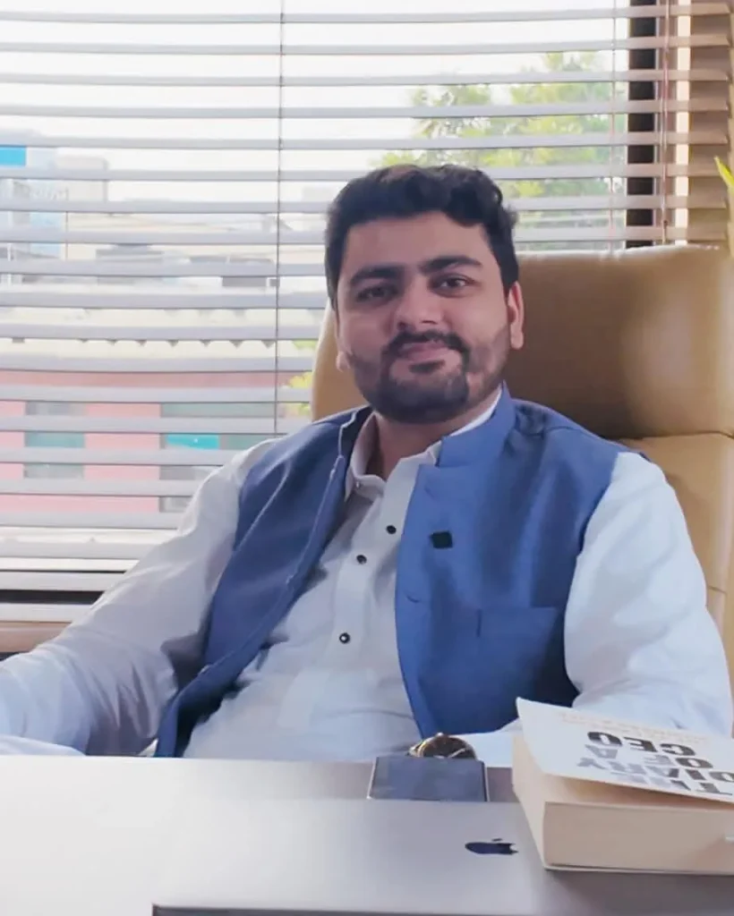 Umar Hameed seated at an office desk in a navy waistcoat and white shirt, smiling