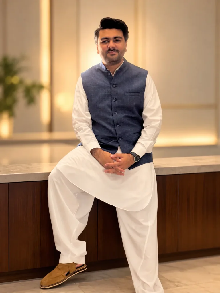 Umar Hameed seated in a navy vest and white shalwar kameez, portrait