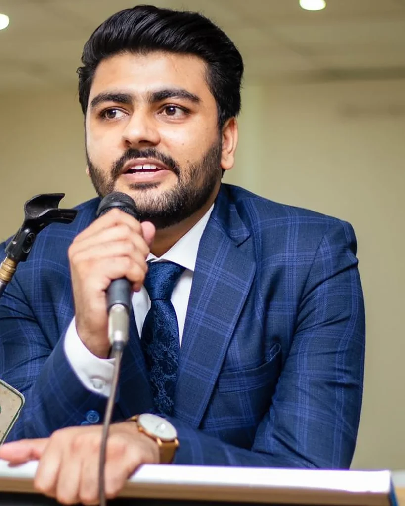 Umar Hameed in a navy check suit speaking into a microphone at a podium