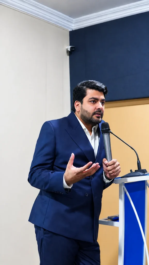 Umar Hameed speaking at a podium with a microphone, gesturing with one hand
