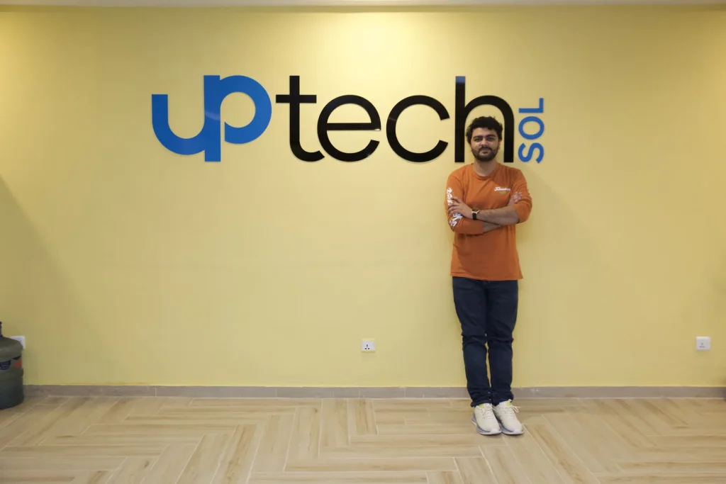 Umar Hameed standing with arms crossed in front of the Uptech Sol logo on a yellow wall